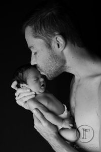 padre besando a su hija en la frente en blanco y negro sobre fondo negro