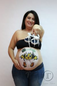 mujer embarazada mostrando unos zapatos de bebe con su barriga pintada con belly painting